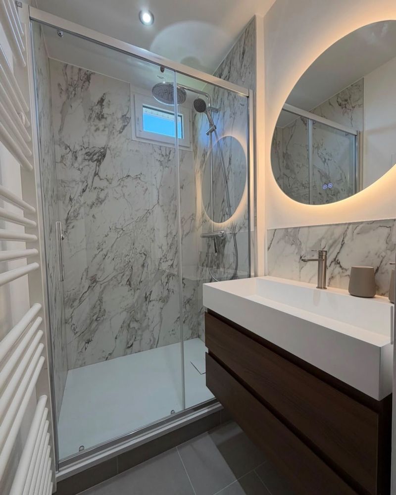 Après rénovation : salle de douche marbre avec miroir rond rétroéclairé